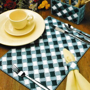 May include: A set of green and white checkered placemats with a matching napkin ring and utensil holder. The placemats are made of plastic canvas and are perfect for adding a touch of country charm to your dining table.