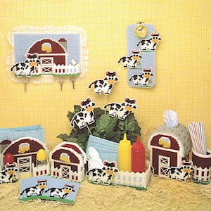 May include: A set of farmhouse-themed kitchen decor featuring a red barn, white picket fence, and black and white cows. The set includes a tissue box cover, napkin holder, utensil holder, and a set of coasters.