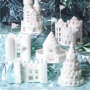 Puede incluir: Una colección de castillos y torres blancos de lona de plástico, cada uno con detalles arquitectónicos únicos. Algunas estructuras presentan pequeñas banderas en sus torres, sobre un fondo plateado reflectante. Los castillos varían en tamaño y diseño.
