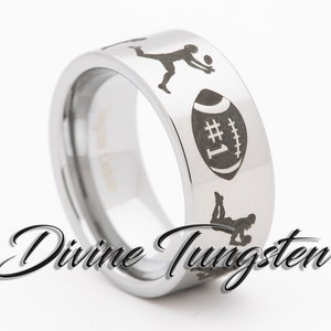 Op de afbeelding: Een zilveren ring van wolfraam met een zwart gegraveerd ontwerp van een voetbal, een volleybalspeler en een voetballer. De ring is gegraveerd met het nummer "#1".