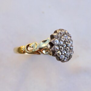 May include: A vintage ring with a cluster of small, clear gemstones set in a silver-toned metal. The ring has a gold-toned band and decorative gold-toned leaves. The gemstones are arranged in a floral pattern.