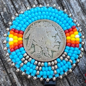 May include: A blue beaded badge holder with a silver-toned buffalo nickel coin in the centre. The coin has the words "Liberty" and "1935" on it. The badge holder has a black retractable cord.