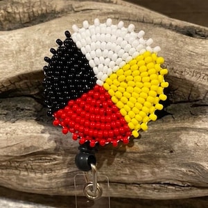 May include: A beaded Native American medicine wheel with black, red, yellow, and white beads. The wheel is attached to a clear plastic badge holder with a black clip.