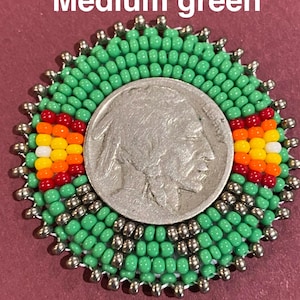 May include: A circular beaded medallion featuring a central silver Buffalo nickel coin surrounded by medium green, metallic silver, red, orange, yellow, and white seed beads. The text Medium green is visible at the top of the image.