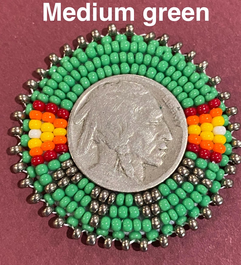 May include: A circular beaded medallion featuring a central silver Buffalo nickel coin surrounded by medium green, metallic silver, red, orange, yellow, and white seed beads. The text Medium green is visible at the top of the image.