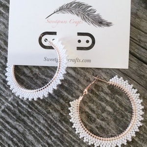 May include: A pair of white beaded hoop earrings with rose gold hoops. The earrings are large and have a delicate, feminine look.