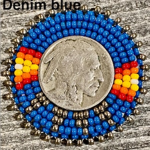 May include: A circular beaded medallion featuring a central silver-toned Buffalo nickel coin. The coin is surrounded by concentric rings of vibrant denim blue seed beads, accented with two rectangular patterns of red, orange, yellow, and white beads.