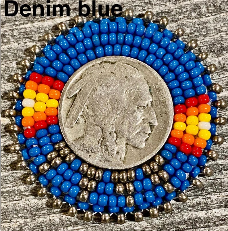 May include: A circular beaded medallion featuring a central silver-toned Buffalo nickel coin. The coin is surrounded by concentric rings of vibrant denim blue seed beads, accented with two rectangular patterns of red, orange, yellow, and white beads.