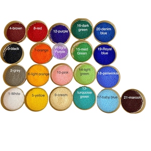 May include: A collection of twenty-one round containers filled with small, uniform beads in various colors, each labeled with a number and color name including white, grey, black, brown, yellow, orange, pink, cream, purple, green, blue, and maroon.
