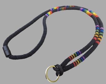 Op de afbeelding: Een zwarte lanyard met een regenboogstreepontwerp en een gouden sleutelhanger.