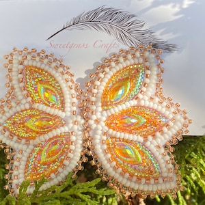 Pode incluir: Um par de brincos de contas brancas e douradas com um design floral. Os brincos são feitos com contas iridescentes e têm um visual delicado e feminino.