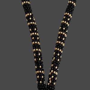 Pode incluir: Um cordão de contas com contas pretas e douradas alternadas. O cordão tem um porta-chaves dourado na parte inferior e é conectado com tecido preto. O texto "-Sweetgrasscrafts.com-" é visível.