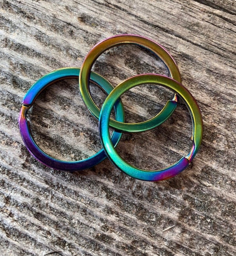 Op de afbeelding: Drie regenboogkleurige sleutelringen in tinten groen, blauw en paars. De ringen zijn van metaal en zijn op elkaar gestapeld.