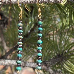 May include: A pair of long, gold dangle earrings with alternating turquoise and black beads.