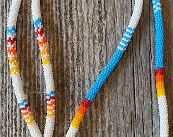 Op de afbeelding: Een wit kralenkoord met een blauw, oranje, rood en geel patroon. Het koord heeft een metalen sluiting en een witte plastic schuif.