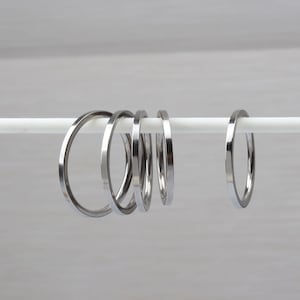 Könnte beinhalten: Ein Satz von sechs silberfarbenen Metallringen, die an einer weißen Stange hängen. Die Ringe sind alle gleich groß und gleich geformt und in einer Reihe angeordnet.