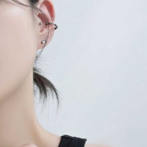 Op de afbeelding: Een close-up van iemands oor met meerdere zilveren oorpiercings. De piercings omvatten een oorring, een oorbel en een helix piercing.