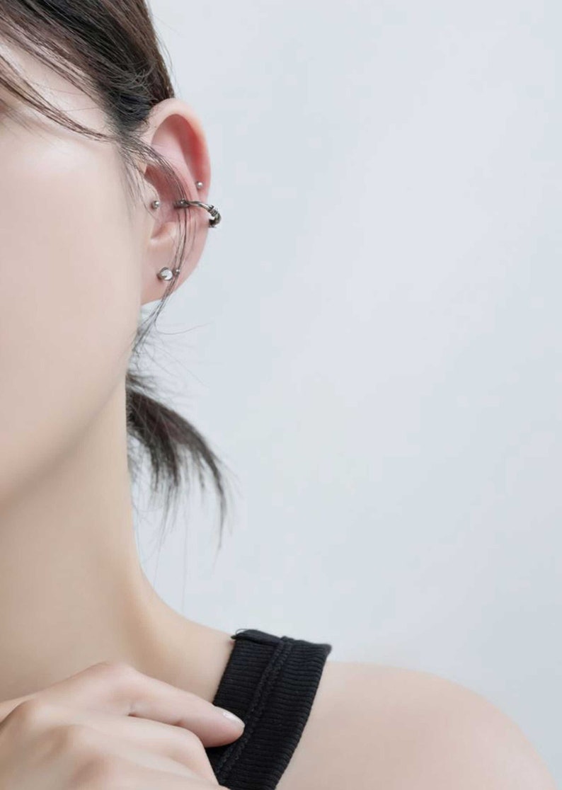 Op de afbeelding: Een close-up van iemands oor met meerdere zilveren oorpiercings. De piercings omvatten een oorring, een oorbel en een helix piercing.