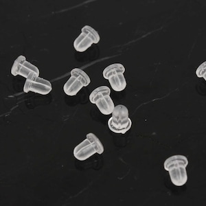 May include: A group of small, clear plastic earring backs scattered on a black surface.