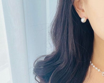 May include: A woman wearing a black shirt with a pearl necklace and pearl earrings.