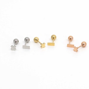 Peut inclure: Trois paires de boucles d'oreilles avec différentes finitions métalliques. Chaque boucle d'oreille a une petite boule à une extrémité et une petite croix ou un rectangle à l'autre extrémité.