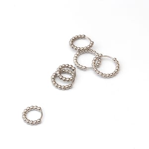 May include: Several small, silver-colored hoop earrings, each adorned with tiny, round beads. The earrings are scattered on a white background, showcasing their simple, yet elegant design. The beads give the earrings a textured appearance.
