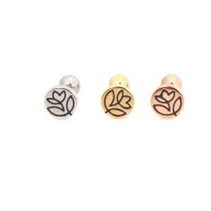 May include: Three silver, gold, and rose gold flower stud earrings with a black outline. The flower design is a stylized tulip.