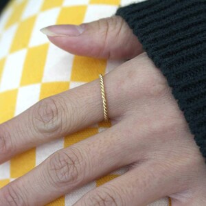 Può includere: Un sottile anello d'oro con un design intrecciato. L'anello è indossato al dito di una persona.