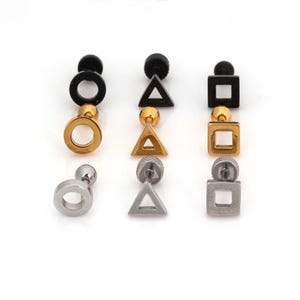 Könnte beinhalten: Drei Paar geometrische Ohrstecker. Jedes Paar hat eine andere Form: ein Kreis, ein Dreieck und ein Quadrat. Die Ohrringe sind in Schwarz-, Gold- und Silbertönen gehalten, mit einem Kugelpfosten.