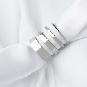 以下が含まれることがあります： 5つの銀色のリングが積み重ねられています。リングはすべてサイズと形が異なり、滑らかで光沢のある金属でできています。