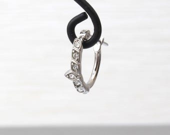 May include: A silver hoop earring with a row of small, clear gemstones set along the outer edge. The earring is suspended from a black hook against a white background. The gemstones are evenly spaced and add a touch of sparkle.