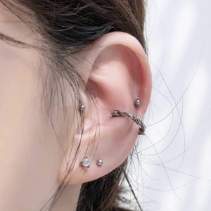 Op de afbeelding: Een oor met meerdere piercings. Het oor is gepierct met een zilveren oorring, een zilveren oorbel en een zilveren barbell piercing.