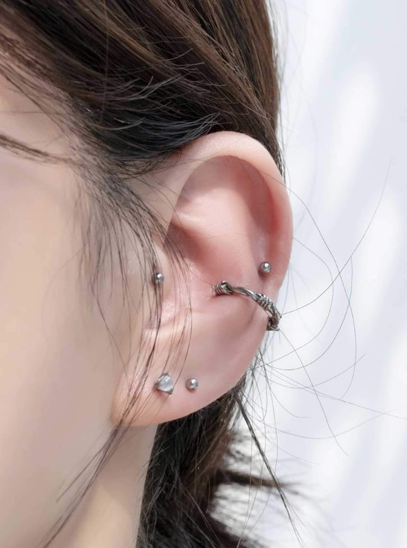 Op de afbeelding: Een oor met meerdere piercings. Het oor is gepierct met een zilveren oorring, een zilveren oorbel en een zilveren barbell piercing.