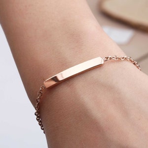 May include: A rose gold bracelet with a thin, rectangular bar charm. The chain is delicate and the bar is smooth.