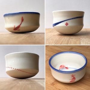 May include: Four white ceramic bowls with blue and red painted designs. The bowls have a rounded shape and are perfect for serving small snacks or desserts.