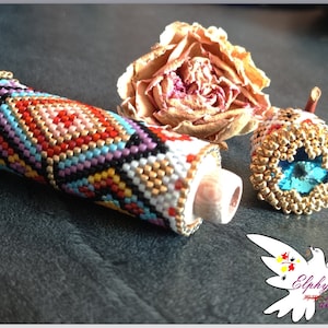 May include: A beaded tube and a beaded ring with a blue stone. The tube is cylindrical with a geometric pattern in red, orange, black, and white beads. The ring has a gold-colored beaded frame.
