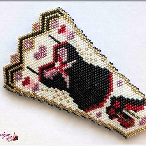 Puede incluir: Horquilla de cuentas con un diseño negro y rojo sobre un fondo blanco, acentuado con detalles florales rosas. Los bordes están delineados con cuentas doradas y negras. La horquilla tiene el texto "Elphy design".