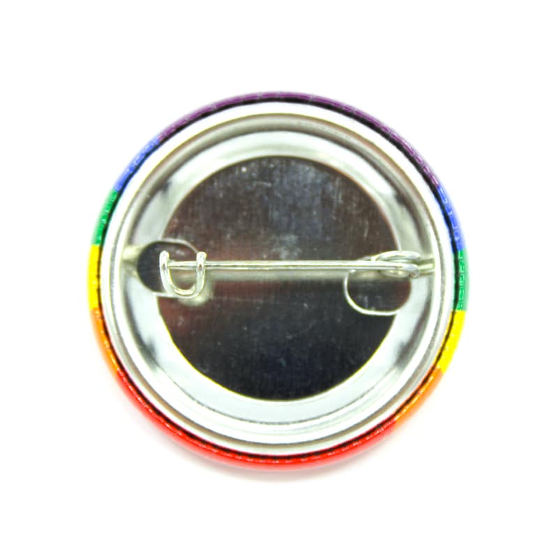 May include: The back of a round button with a rainbow design. The button has a metal pin on the back.