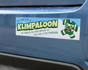 Puede incluir: Una pegatina rectangular con fondo azul claro y siluetas de montañas blancas. Incluye el texto MY OTHER RIDE IS KLIMPALOON THE MAGICAL OLD-TIMEY BATHING SUIT WHO LIVES IN THE HIMALAYAS y una criatura a rayas de color verde y blanco.