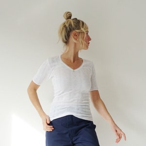 May include: A white V-neck short-sleeve shirt and navy blue pants with rolled-up cuffs. The pants are a loose fit. The outfit is simple and casual.