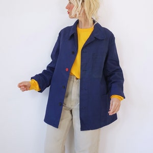 Pu&ograve; includere: Giacca blu navy con bottoni, un bottone rosso e due tasche anteriori. La giacca &egrave; indossata sopra una maglietta gialla a maniche lunghe e abbinata a pantaloni beige. La modella indossa la giacca.
