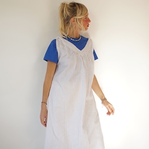 Puede incluir: Un vestido sin mangas de rayas blancas y azules con escote en V. El vestido se lleva sobre una camiseta azul.