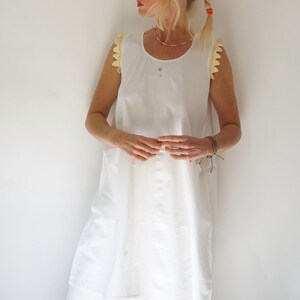 May include: A white sleeveless dress with crochet trim on the shoulders. The dress has a loose fit and a scoop neckline.