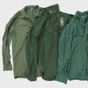 May include: Four green long-sleeved shirts are displayed. The shirts vary in shade, from olive to a darker green. One shirt has a small tag, and another features a small Swedish flag patch on the sleeve. The shirts are made of a lightweight fabric.