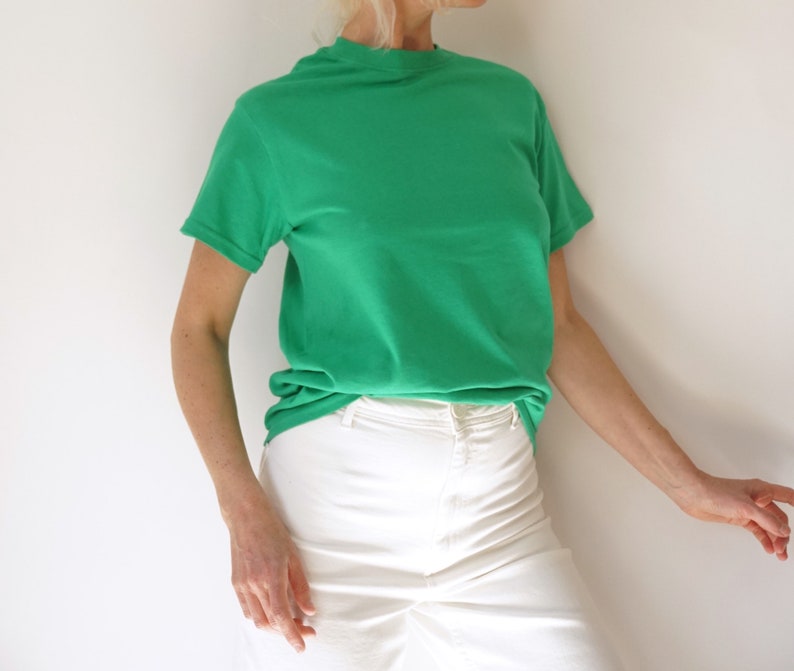 May include: A short-sleeved, emerald green t-shirt paired with white pants. The t-shirt has a crew neck and a relaxed fit. The pants are high-waisted.