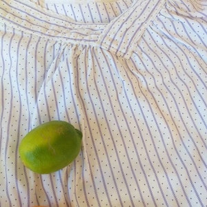 May include: White cotton fabric with thin purple stripes and small white dots. A green lime and an orange are partially visible at the bottom of the image.