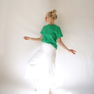 May include: A green crew neck t-shirt and white skirt. The t-shirt is a vibrant green color, and the skirt is a crisp white. The outfit is simple and casual, suitable for everyday wear. The model is wearing the outfit.