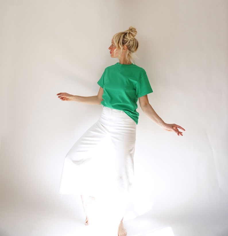 May include: A green crew neck t-shirt and white skirt. The t-shirt is a vibrant green color, and the skirt is a crisp white. The outfit is simple and casual, suitable for everyday wear. The model is wearing the outfit.