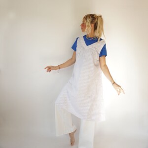 May include: A white and blue striped dress with a V-neckline and a loose fit. The dress is worn over a blue t-shirt and white trousers.