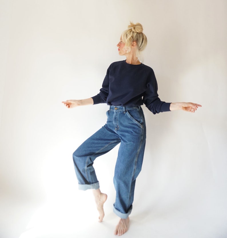May include: A navy blue crew neck sweatshirt and blue denim jeans. The jeans have a classic fit with a straight leg and rolled cuffs. The model is wearing the outfit in front of a white background.